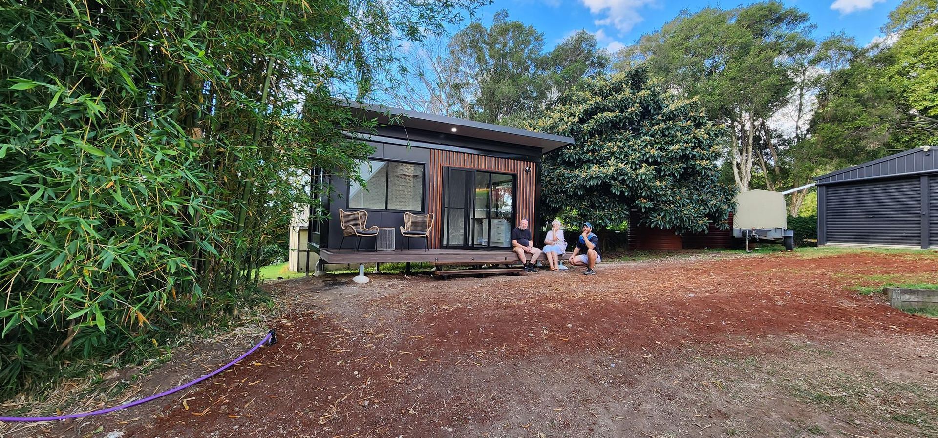 A Group of People Are Sitting Outside of A Small House Surrounded by Trees — Alternative Modular Home In Toowoomba City, QLD
