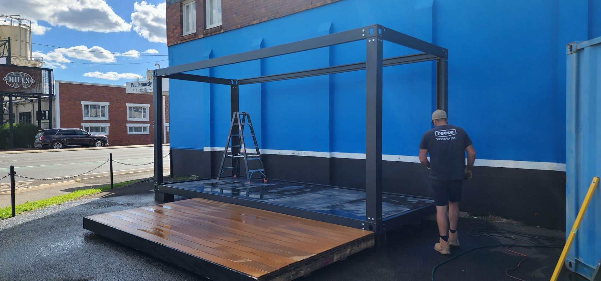 A Man Is Standing in Front of A Blue Building — Alternative Modular Home In Toowoomba City, QLD