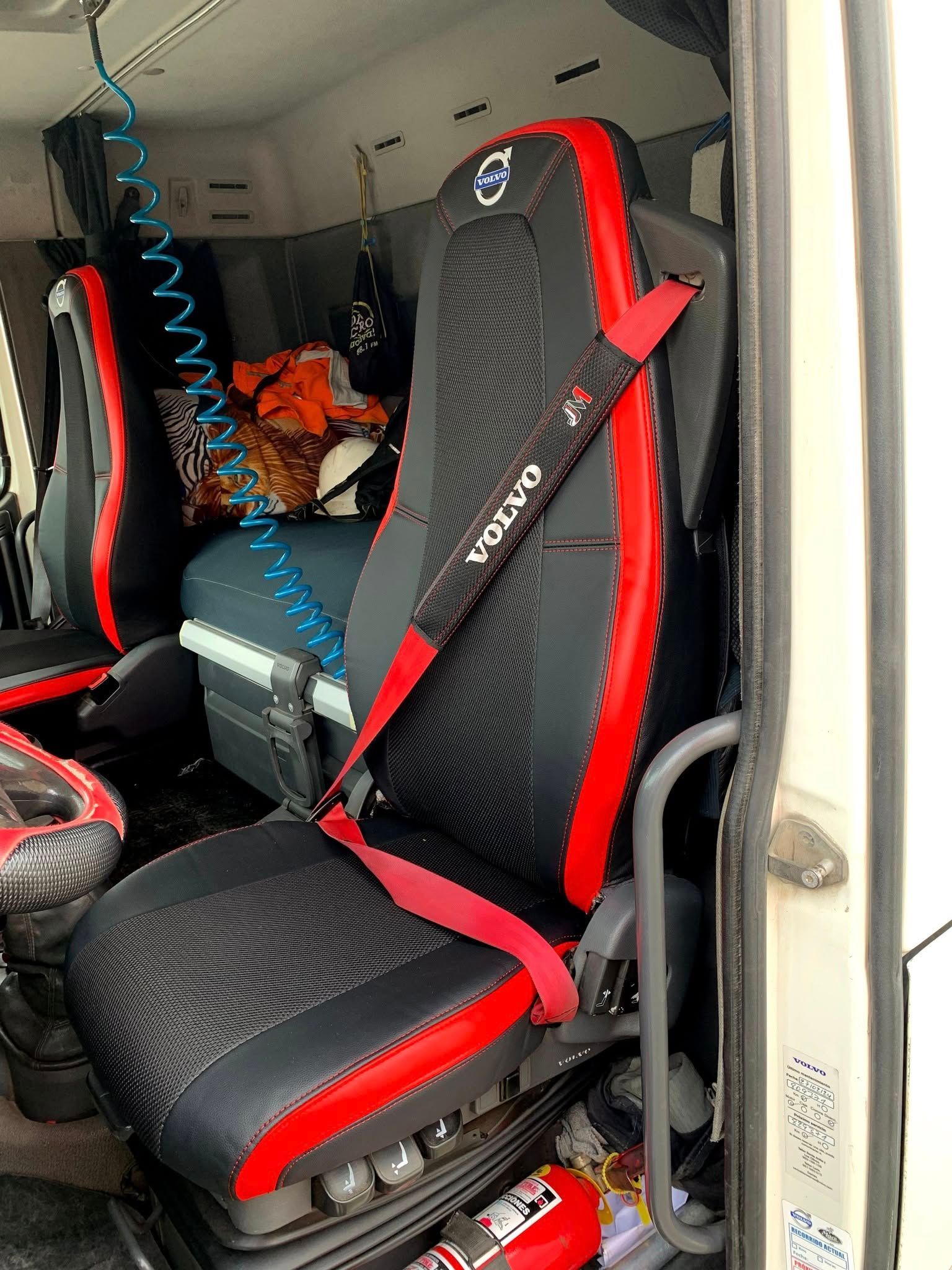 Asiento de estilo deportivo rojo y negro en el interior de la cabina de un vehículo, con equipaje detrás.