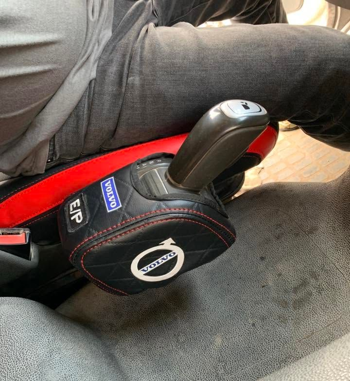 La palanca de cambios de un coche, situada junto al regazo de una persona, con una funda protectora de color negro y rojo.