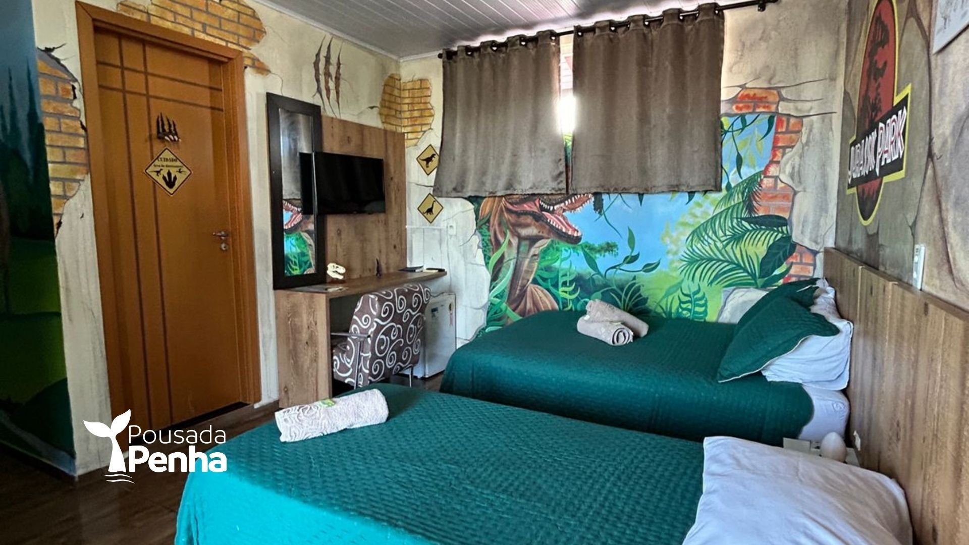 Um quarto com decoração temática de dinossauros, apresentando duas camas com roupa de cama verde e um mural da selva na parede.