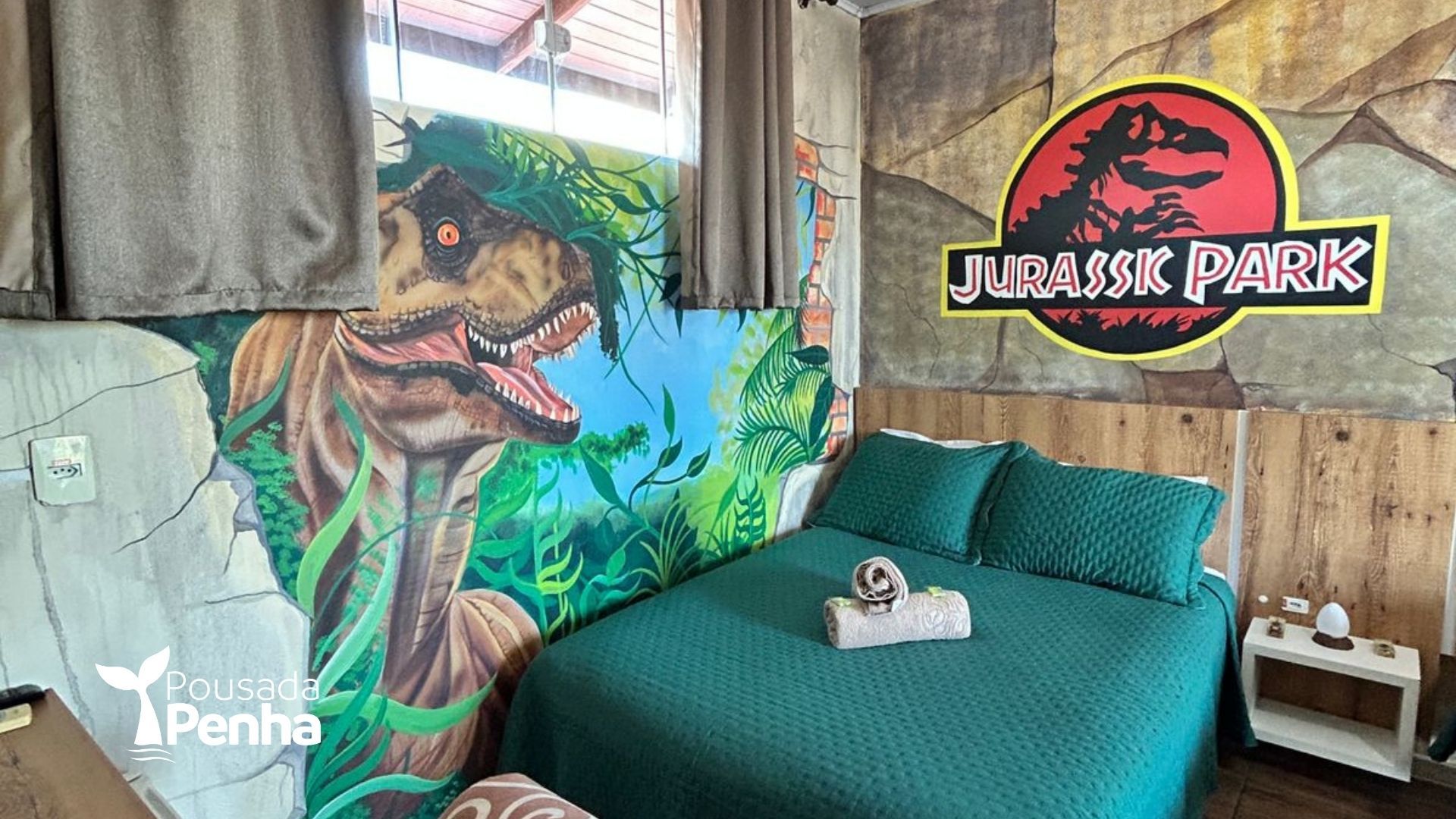 Um quarto temático inspirado em Jurassic Park, com um mural de dinossauros, uma cama verde e o logotipo do filme na parede.