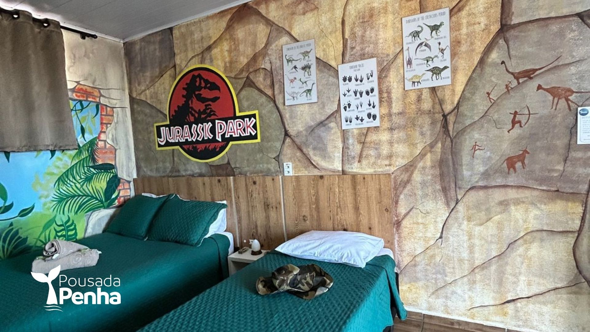 Um quarto de hotel temático do Parque Jurássico com duas camas de solteiro, paredes com textura de pedra e pôsteres e obras de arte com tema de dinossauros.