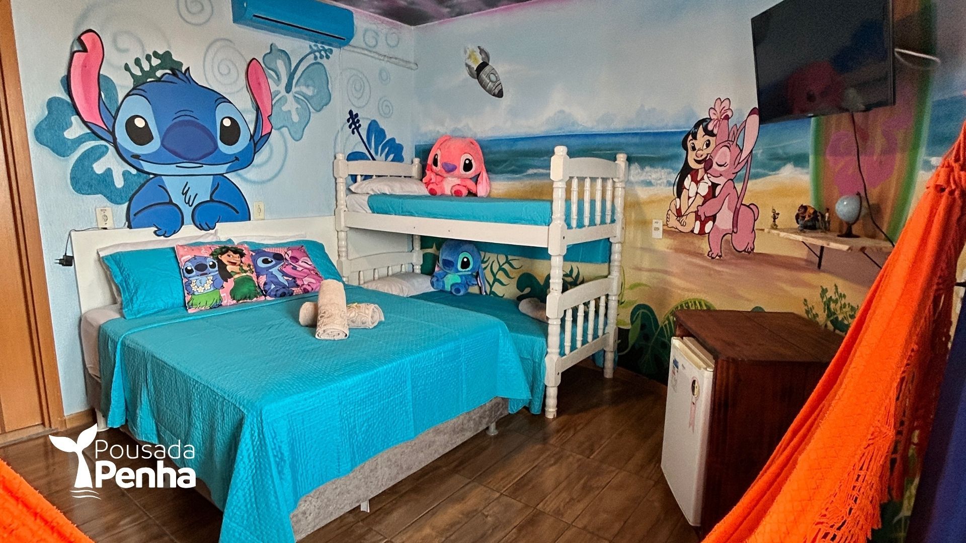 Um quarto temático com Stitch e Angel, apresentando uma cama de casal com roupa de cama azul, um beliche branco e um armário de madeira.