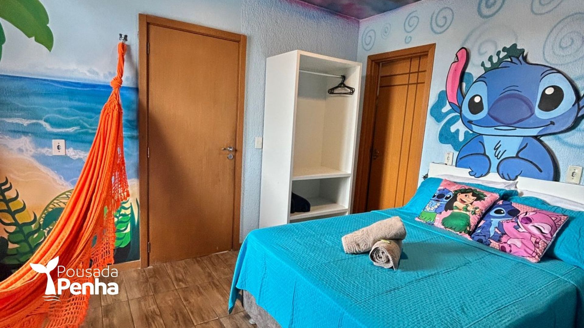 Quarto com uma parede temática do Stitch, colcha azul vibrante, rede laranja e porta de madeira clara.