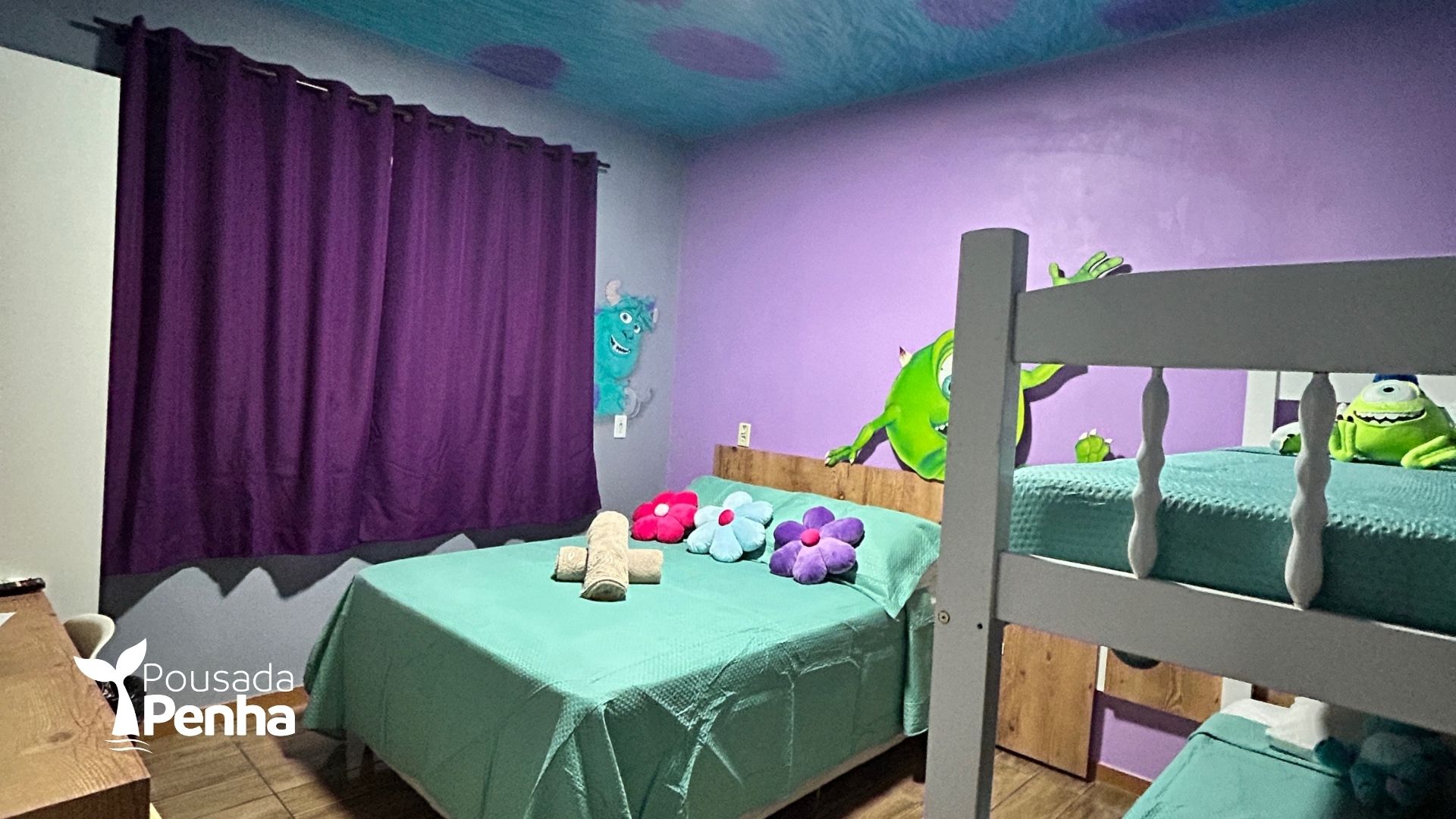 Um quarto infantil com o tema de Monstros S.A., apresentando uma cama, um beliche, cortinas roxas e arte de parede verde brilhante.