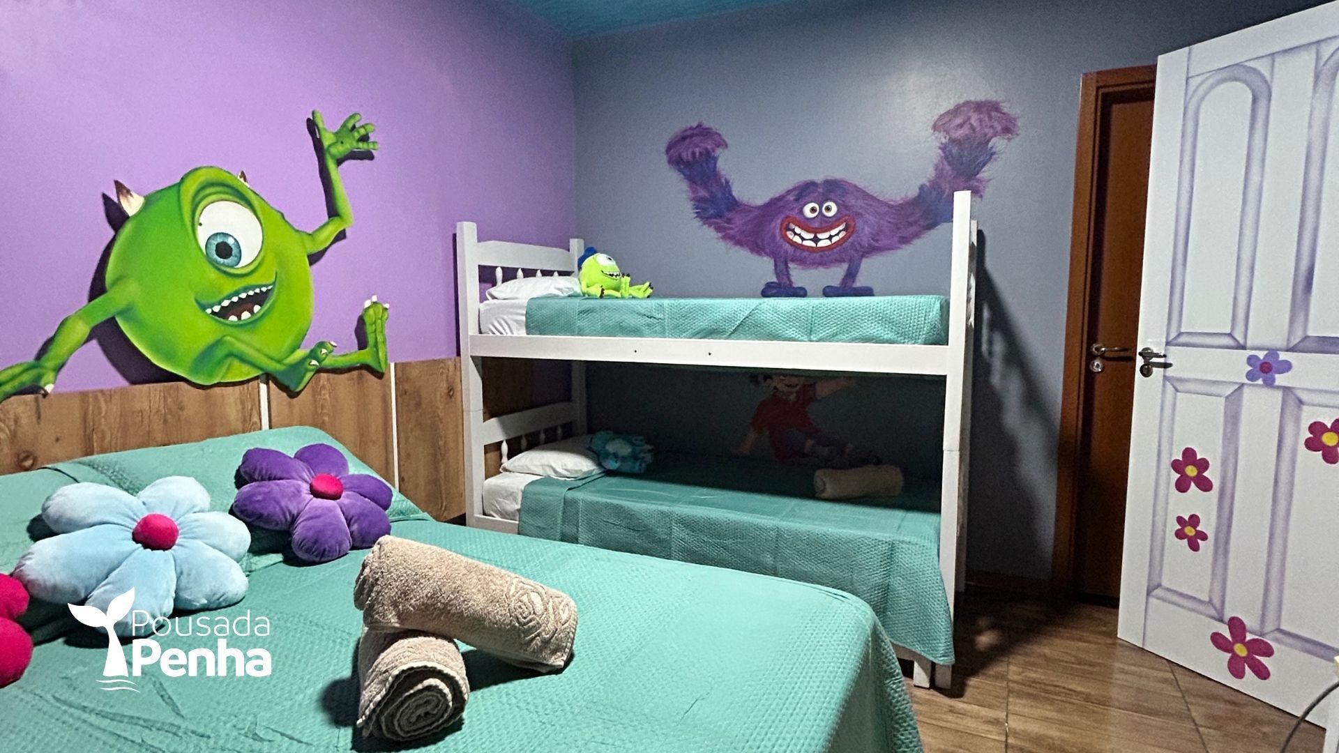 Um quarto temático e colorido com um beliche, uma cama de casal com almofadas em formato de flor e murais de monstros de desenho animado nas paredes.