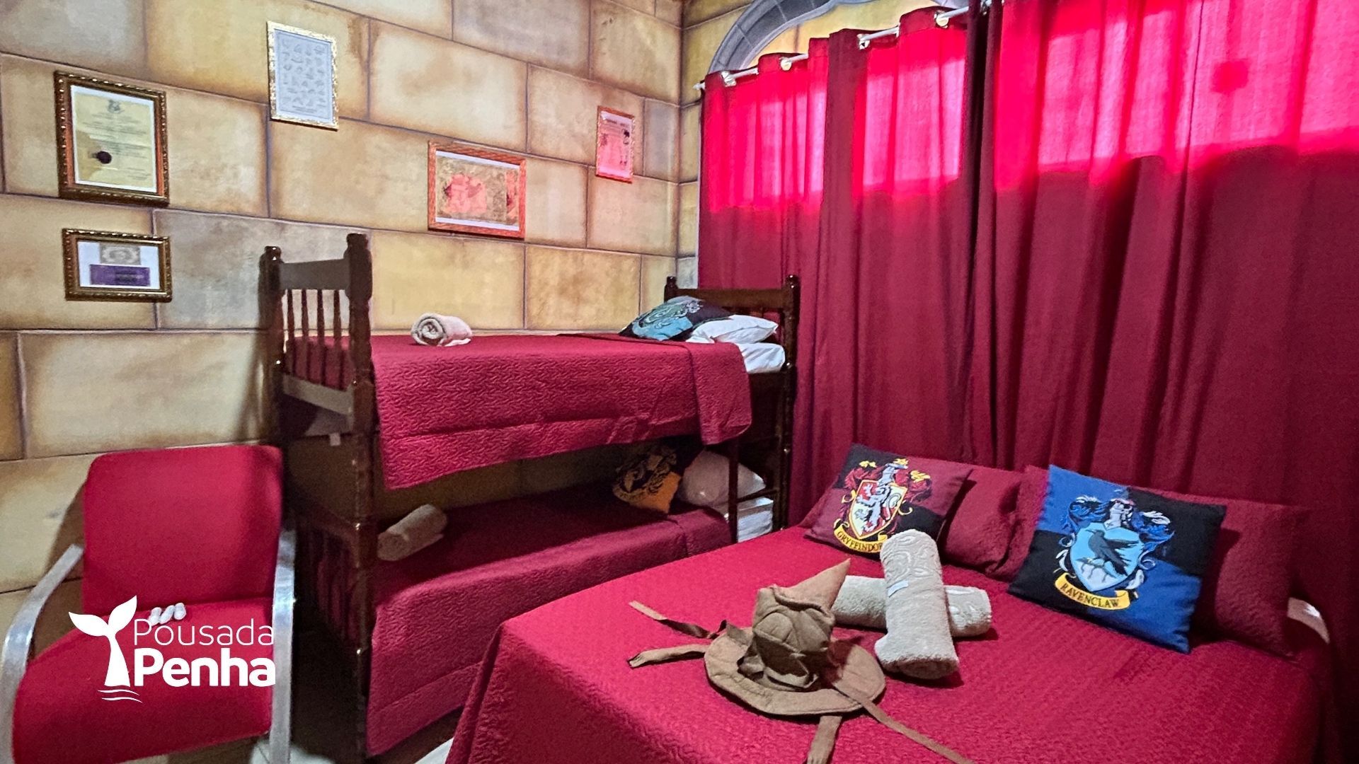 Um quarto temático com beliches, uma cama de casal, roupa de cama vermelha, paredes com estampa de pedra e almofadas inspiradas em Harry Potter.
