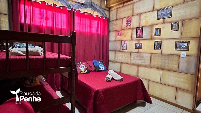 Um quarto de hotel com um beliche e uma cama de casal em tons de vermelho, com papel de parede texturizado que imita pedra e fotos emolduradas.