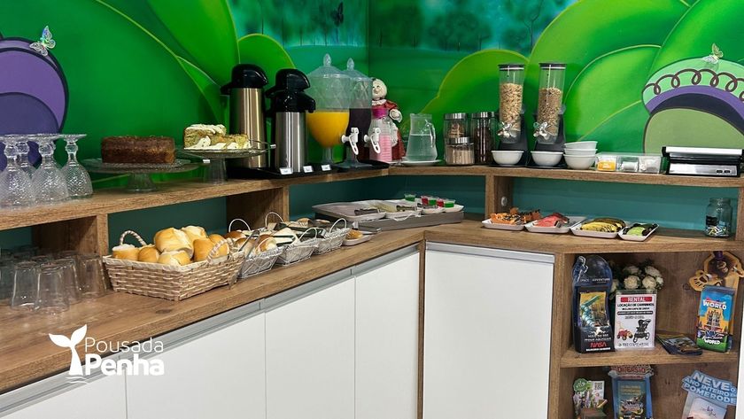 Um buffet de café da manhã com doces, pães, máquinas de café e máquinas de cereais, tendo como pano de fundo um mural verde.