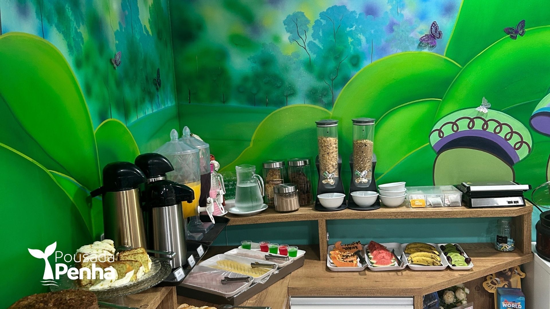 Um buffet de café da manhã com dispensadores de cereais, garrafas térmicas para bebidas e bandejas de comida, tudo isso em uma parede verde com temática da natureza.