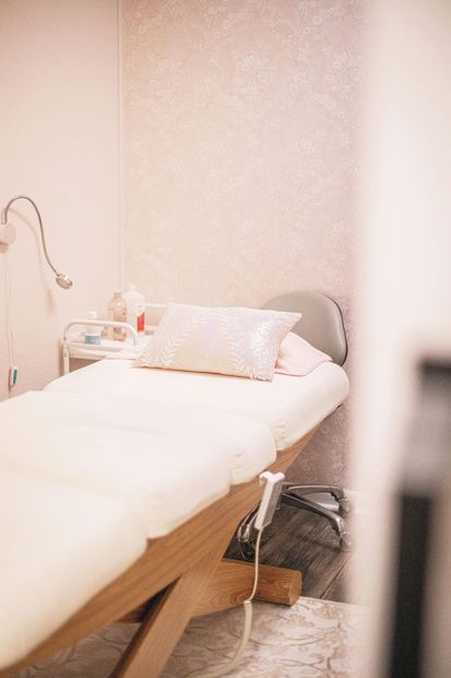 Una camilla de masaje con una almohada blanca en una habitación minimalista con papel pintado de color rosa 