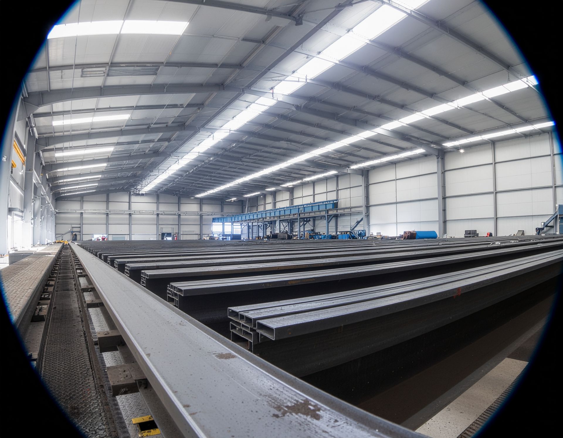 Steel beams stored in a large industrial warehouse with overhead lighting.