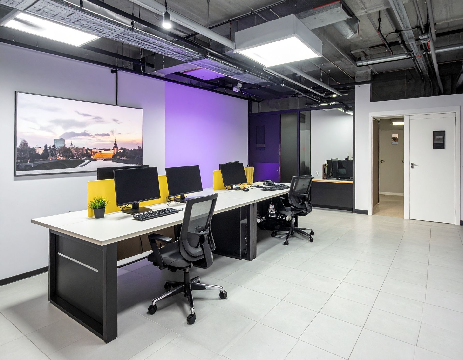 Modern office with desks, computers, and chairs. Purple and white walls, gray floor, and overhead lighting.