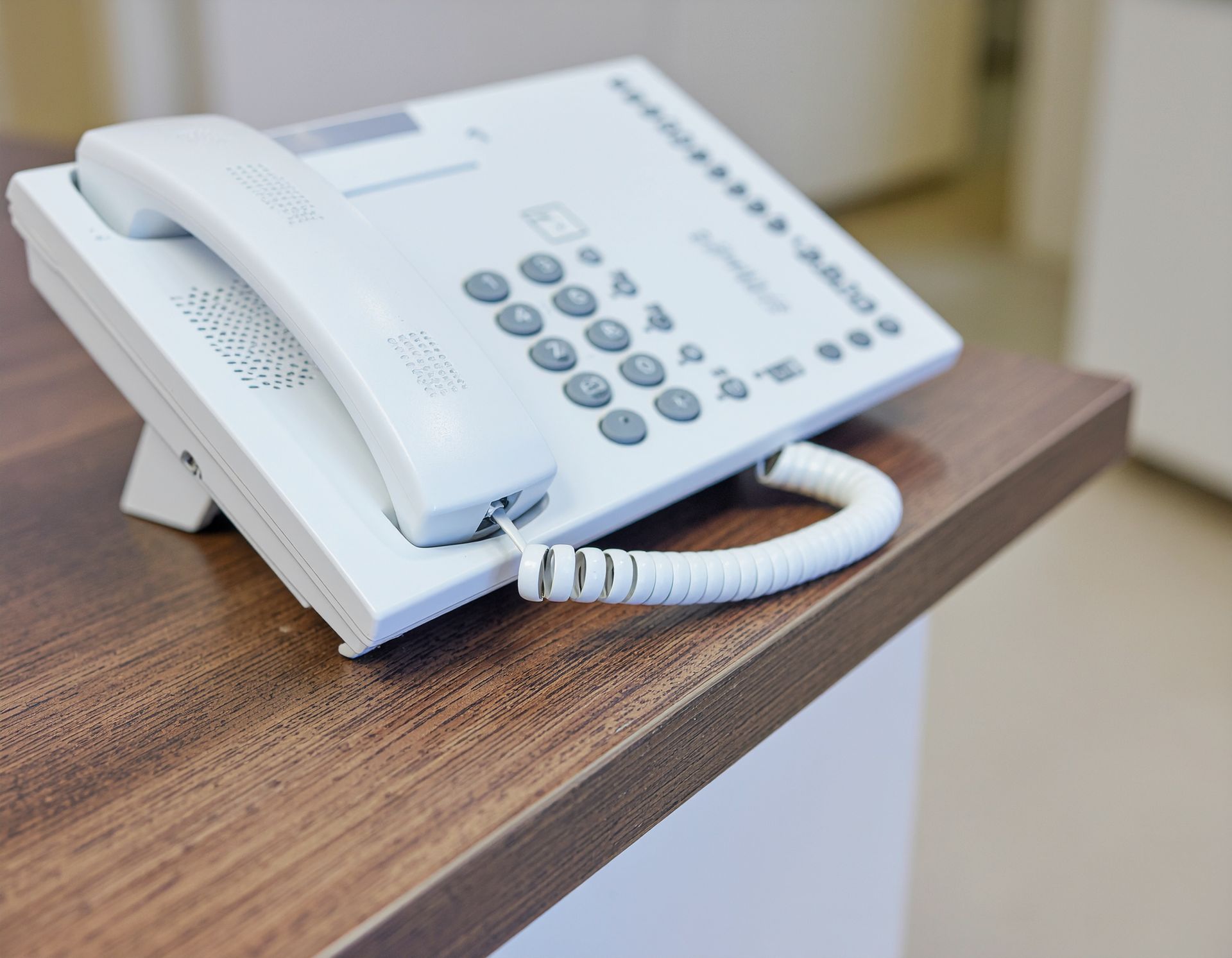 White office phone on a brown wooden desk.