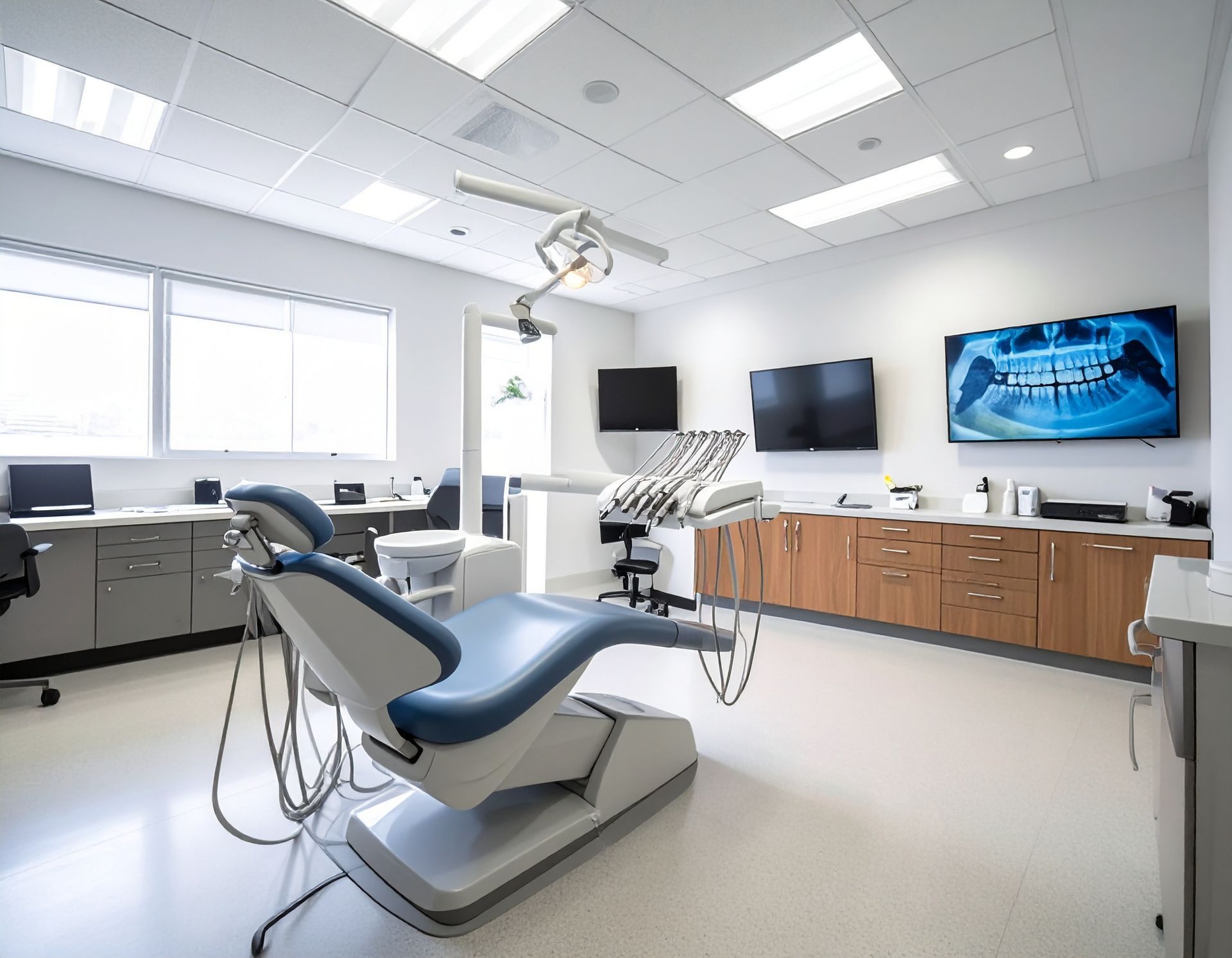Dental office exam room with blue chair, dental equipment, and monitors.