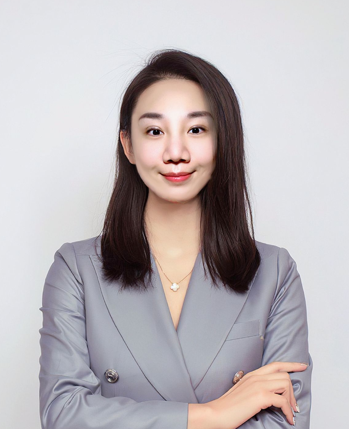 Woman with arms crossed, wearing a gray suit, smiling in front of a white background.