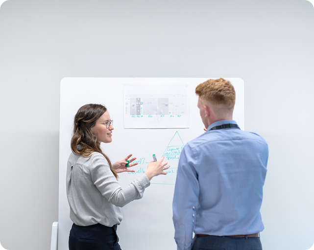 People at a table, collaborating on blueprints in an office with a large screen displaying schematics.
