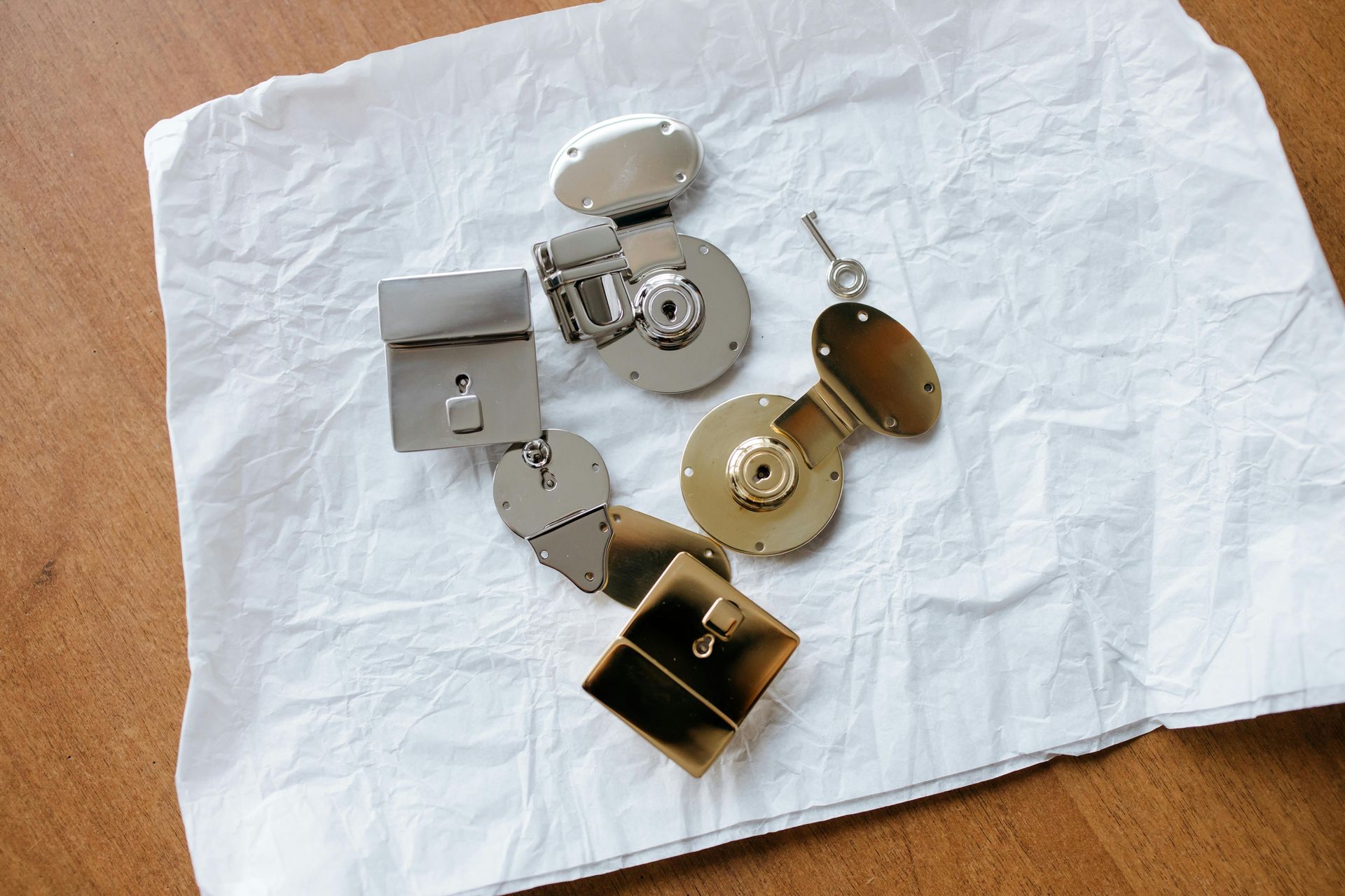 Various metallic clasps and locks on a crumpled white paper, resting on a wooden surface.