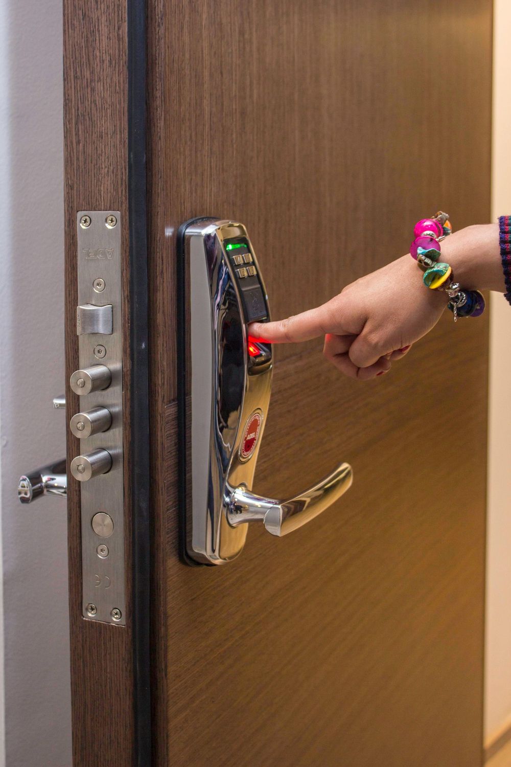 Finger pressing a red button on a smart lock of a brown door with silver handle and lock mechanism.