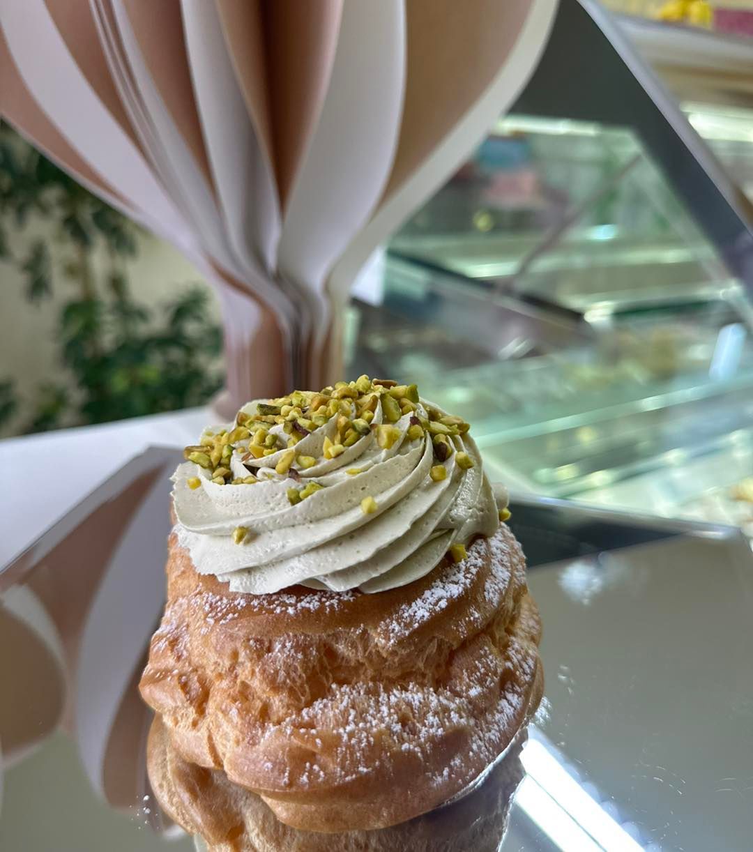 Su un tavolo è appoggiato un dolce con panna montata e pistacchi sopra.