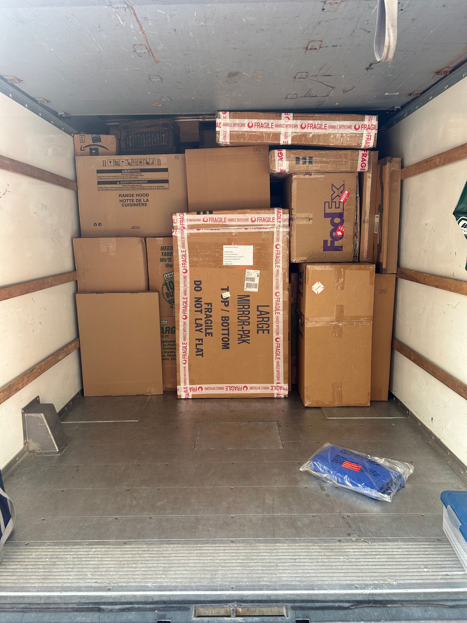 Inside the back of a moving truck, stacked cardboard boxes of various sizes fill the cargo space.