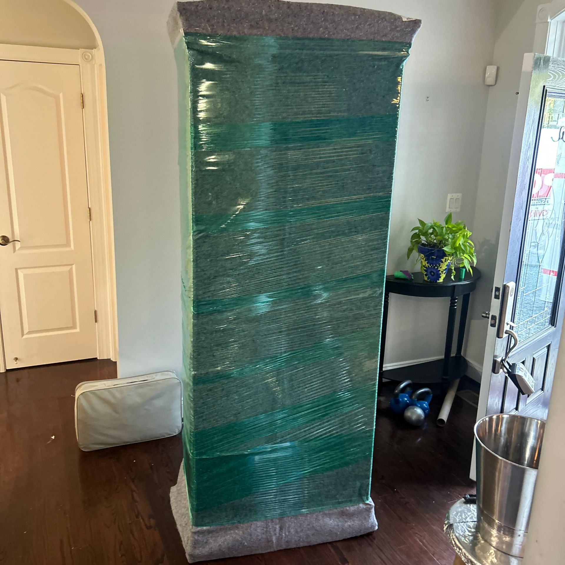 Tall, wrapped object in a hallway, possibly a piece of furniture being moved.