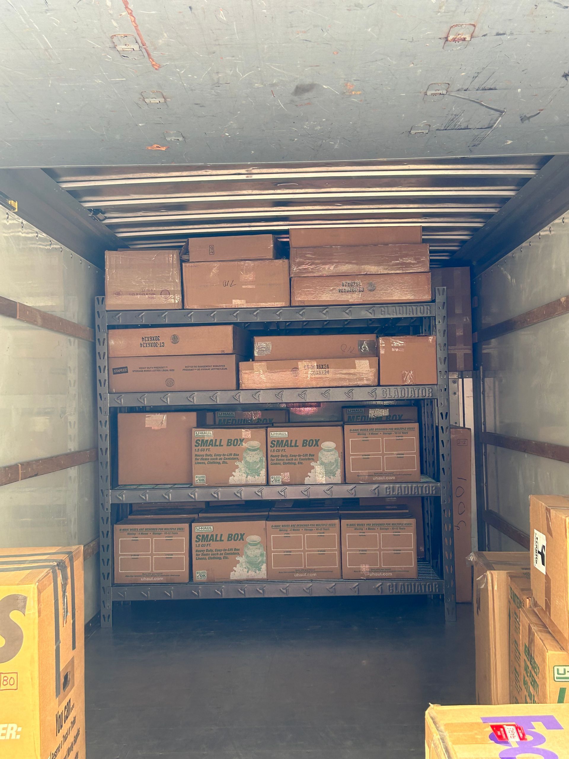 A tall metal shelving unit filled with cardboard shipping boxes inside the back of a delivery truck.