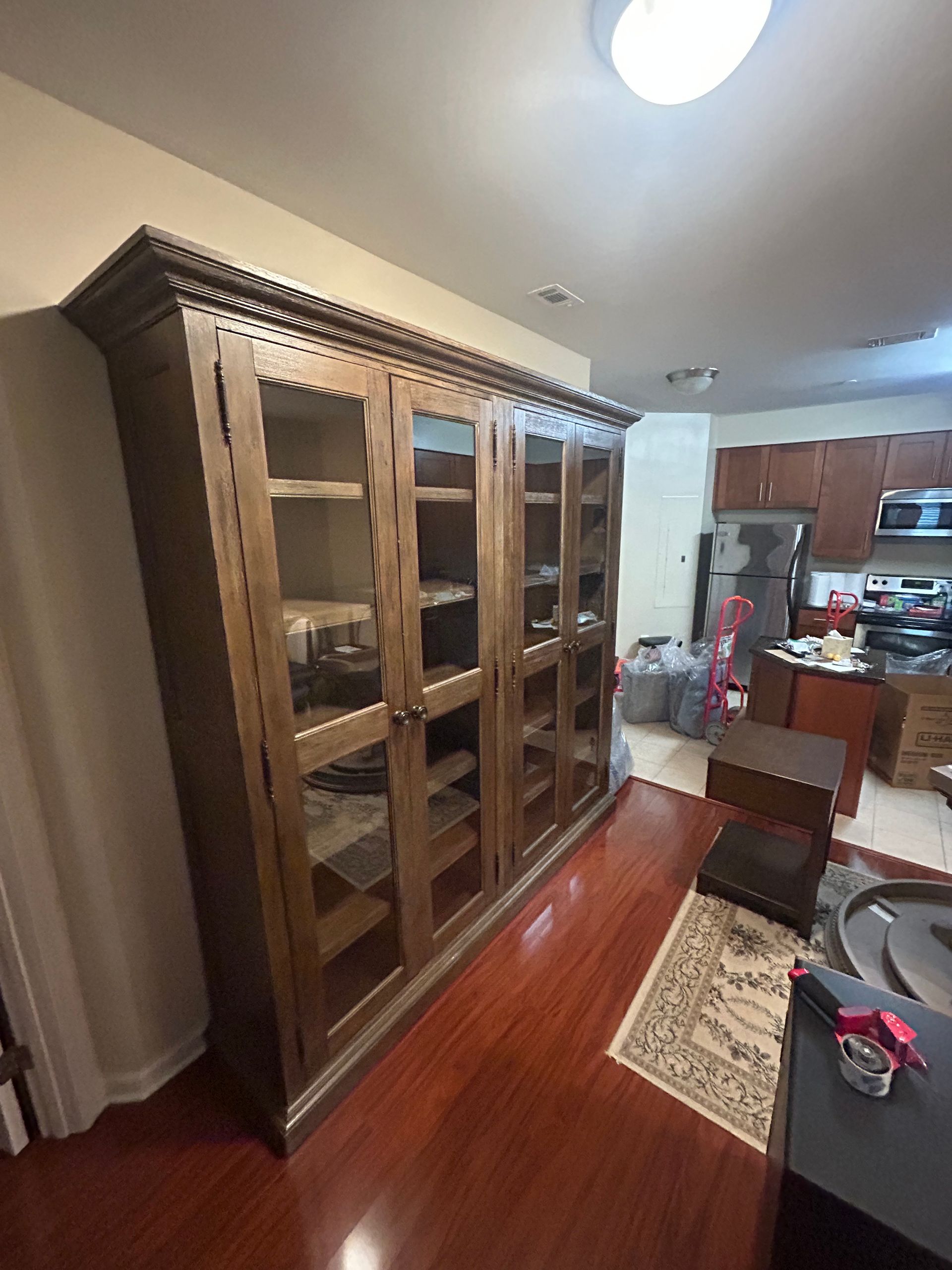 A large, four-door wooden display cabinet with glass panels stands on a polished hardwood floor in a home interior.
