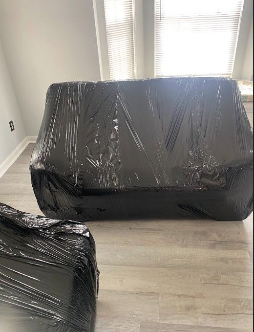 Two black wrapped sofas in a room with a window and light-colored flooring.