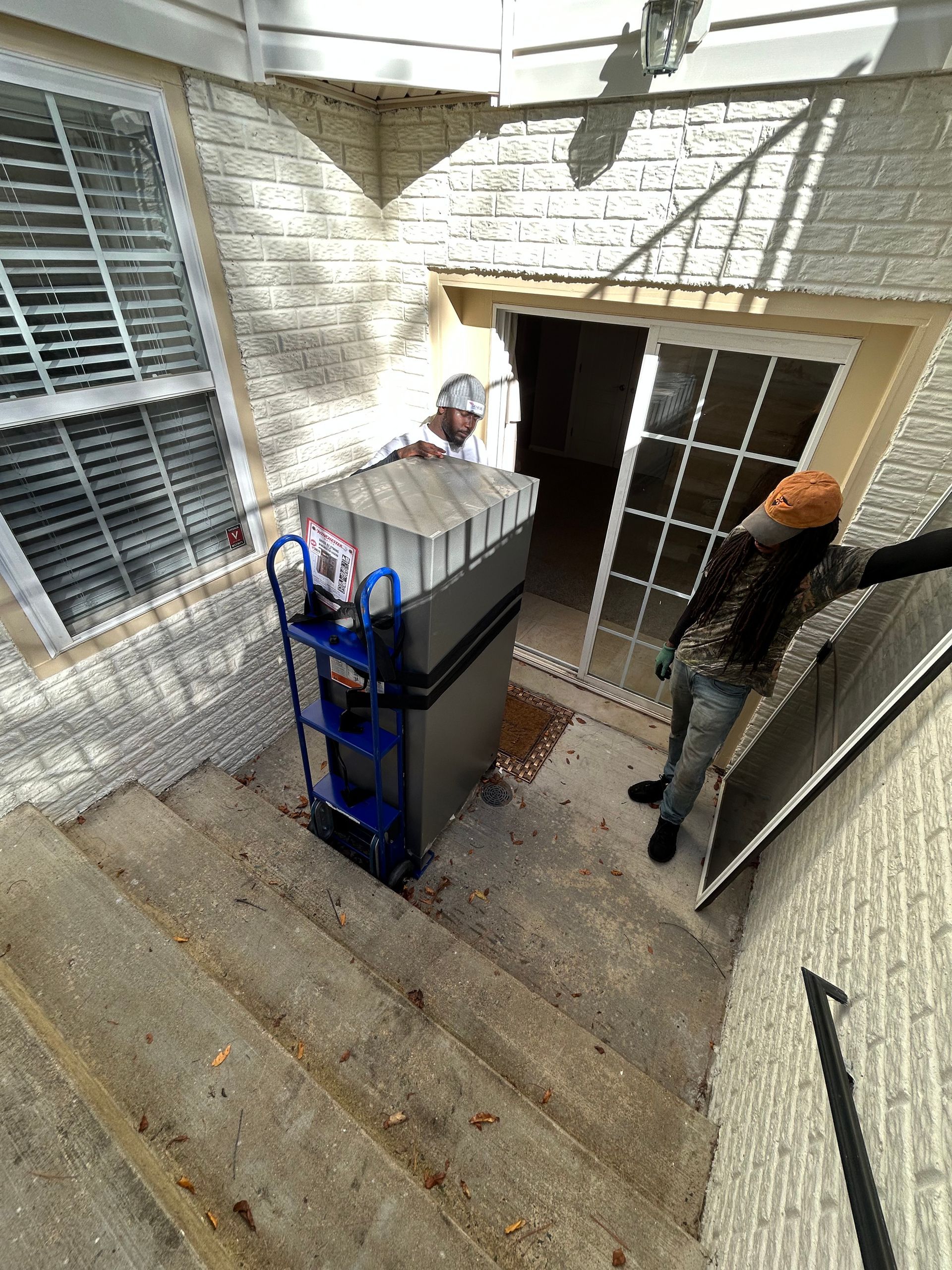 A man is pushing a refrigerator down a set of stairs.