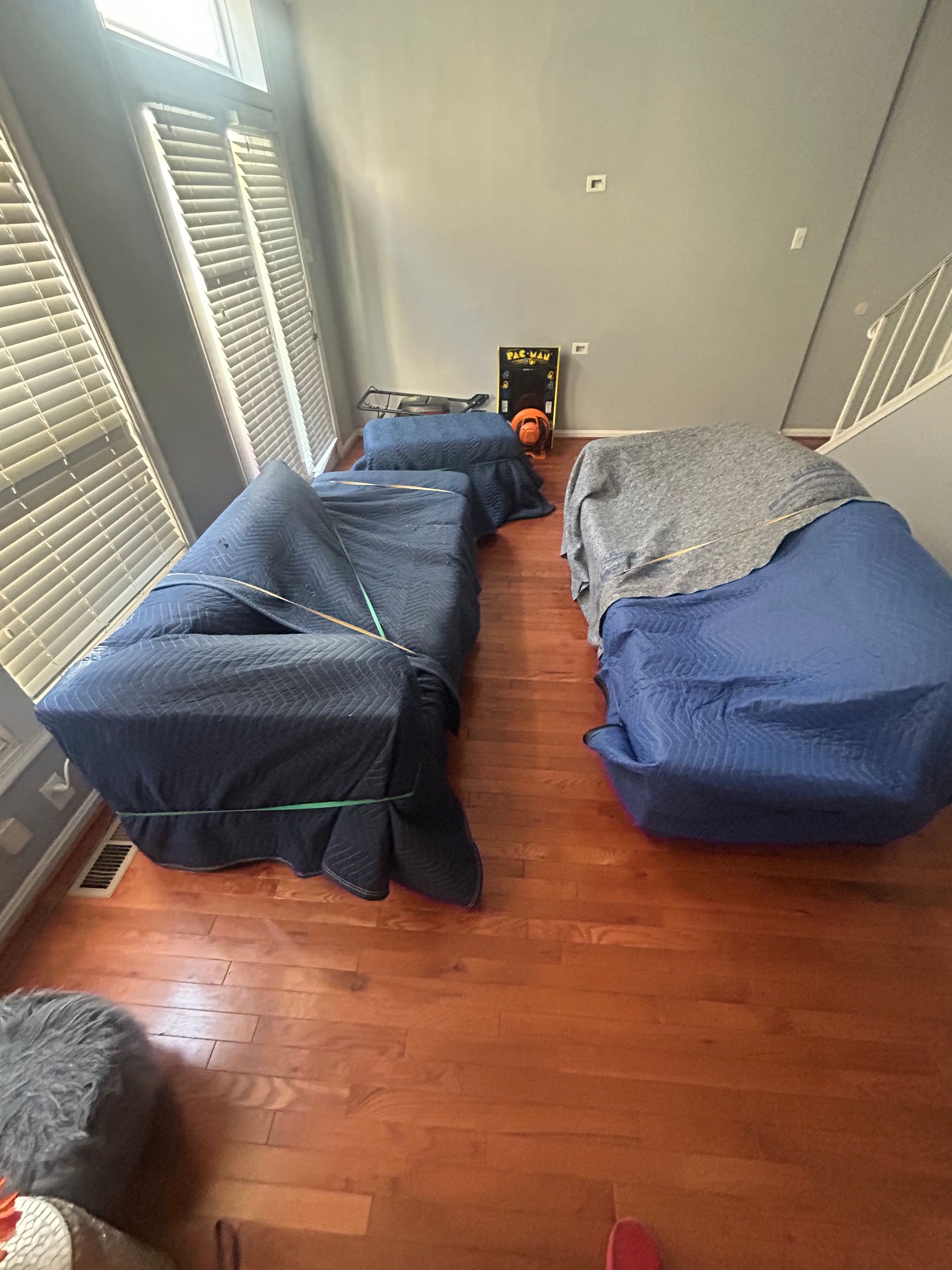 A living room filled with furniture wrapped in blue blankets.