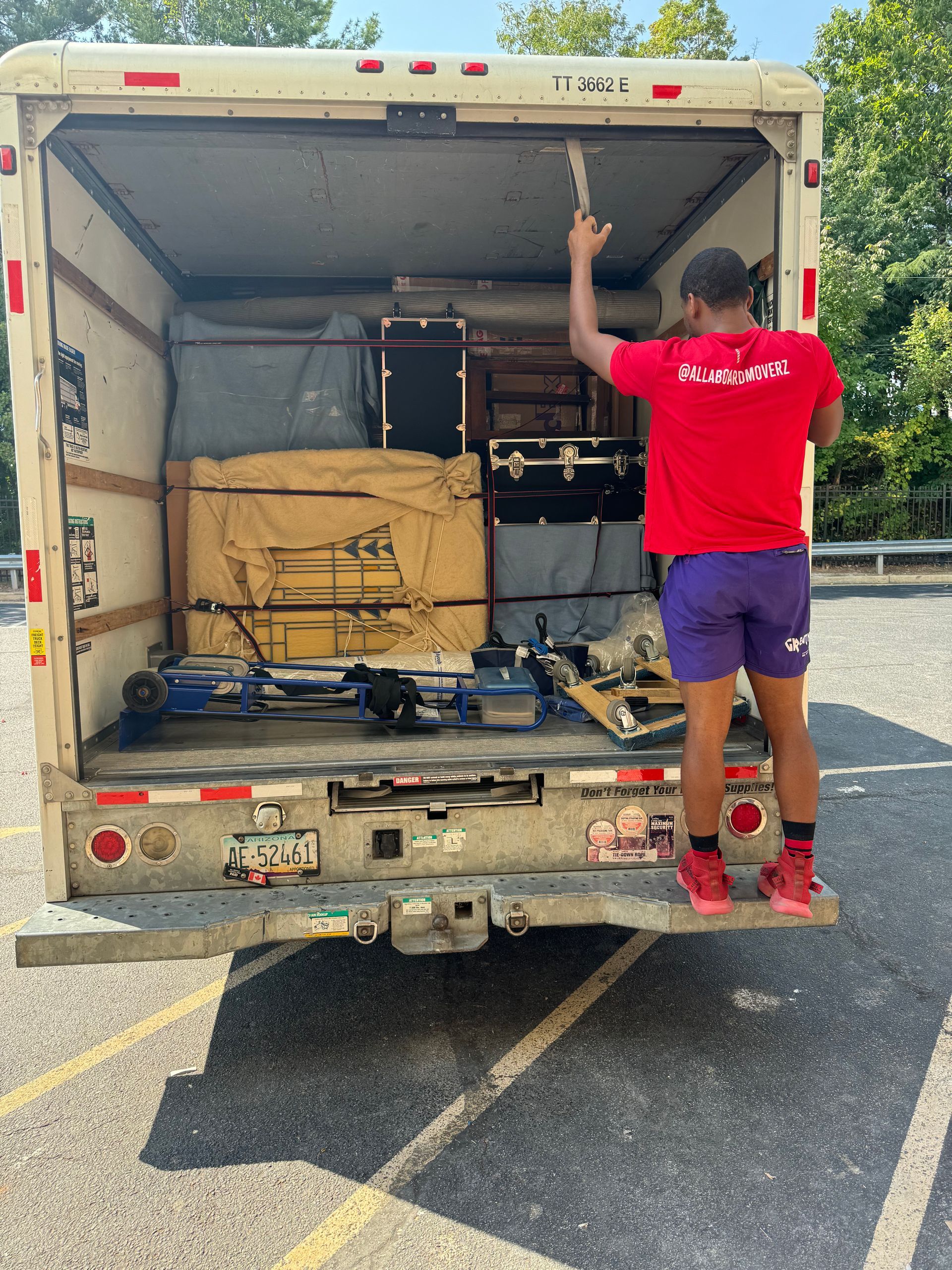 A man in a red shirt is standing in front of a moving truck.