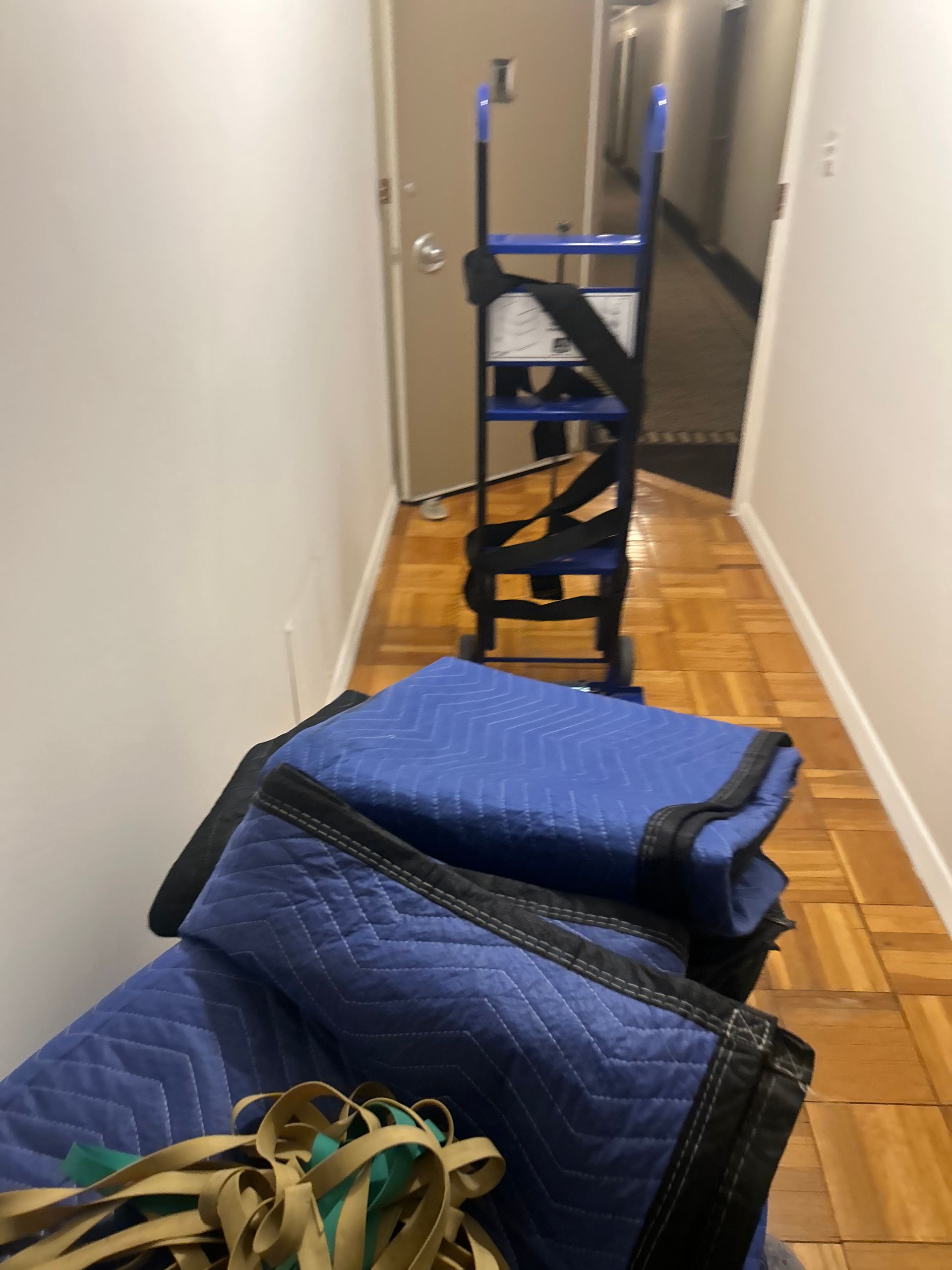 A stack of blue blankets sits in a hallway next to a ladder