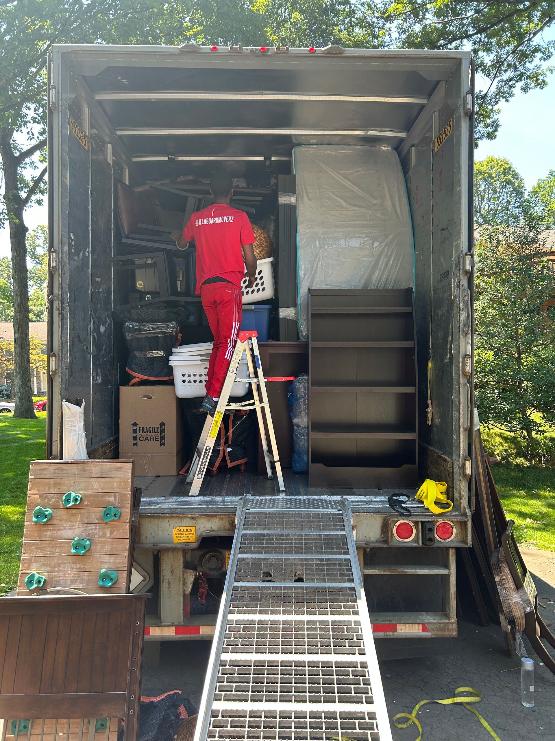 A man in a red shirt is standing in a dining room surrounded by boxes.