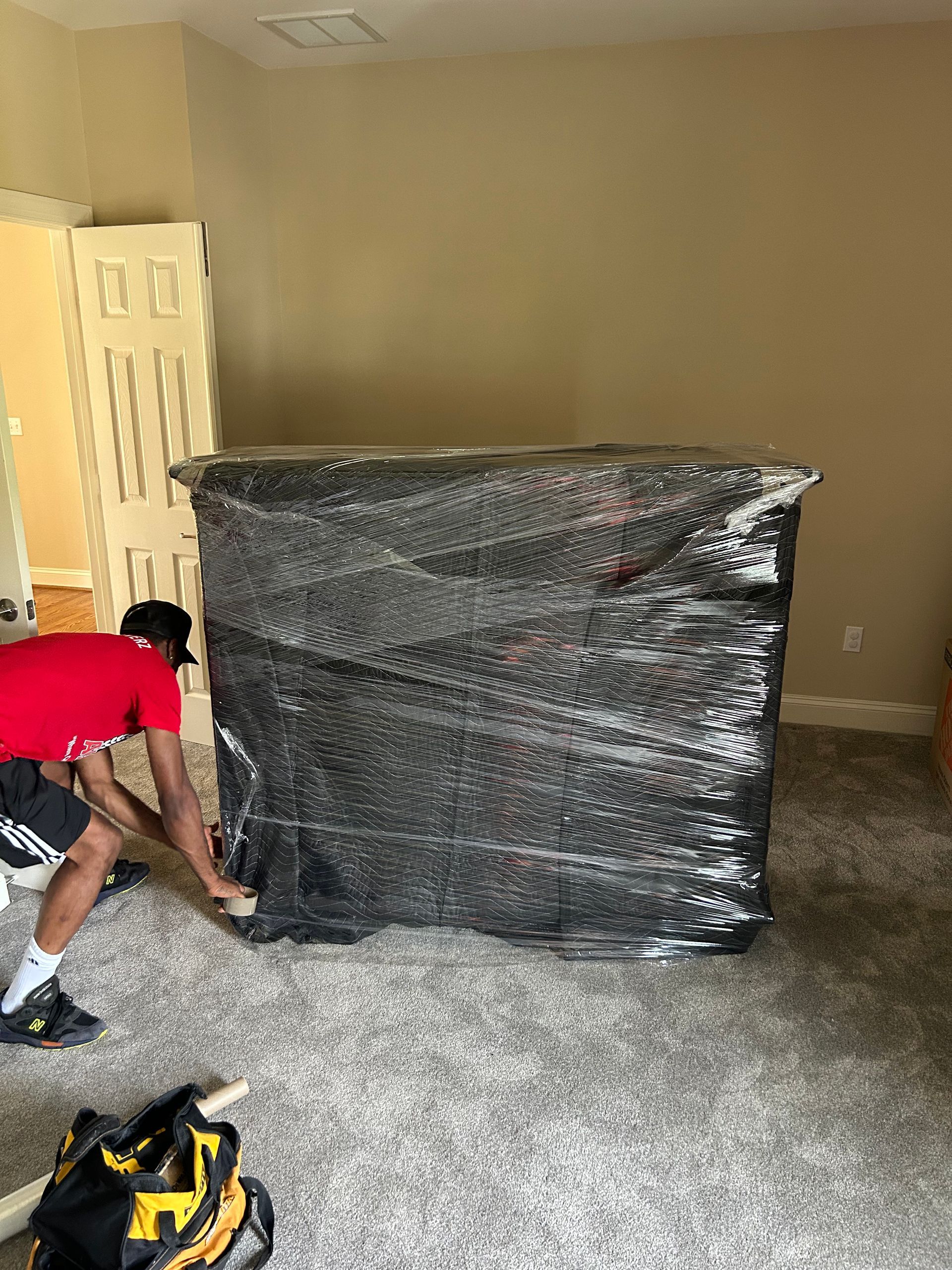 A man is wrapping a mattress in plastic wrap in a room.