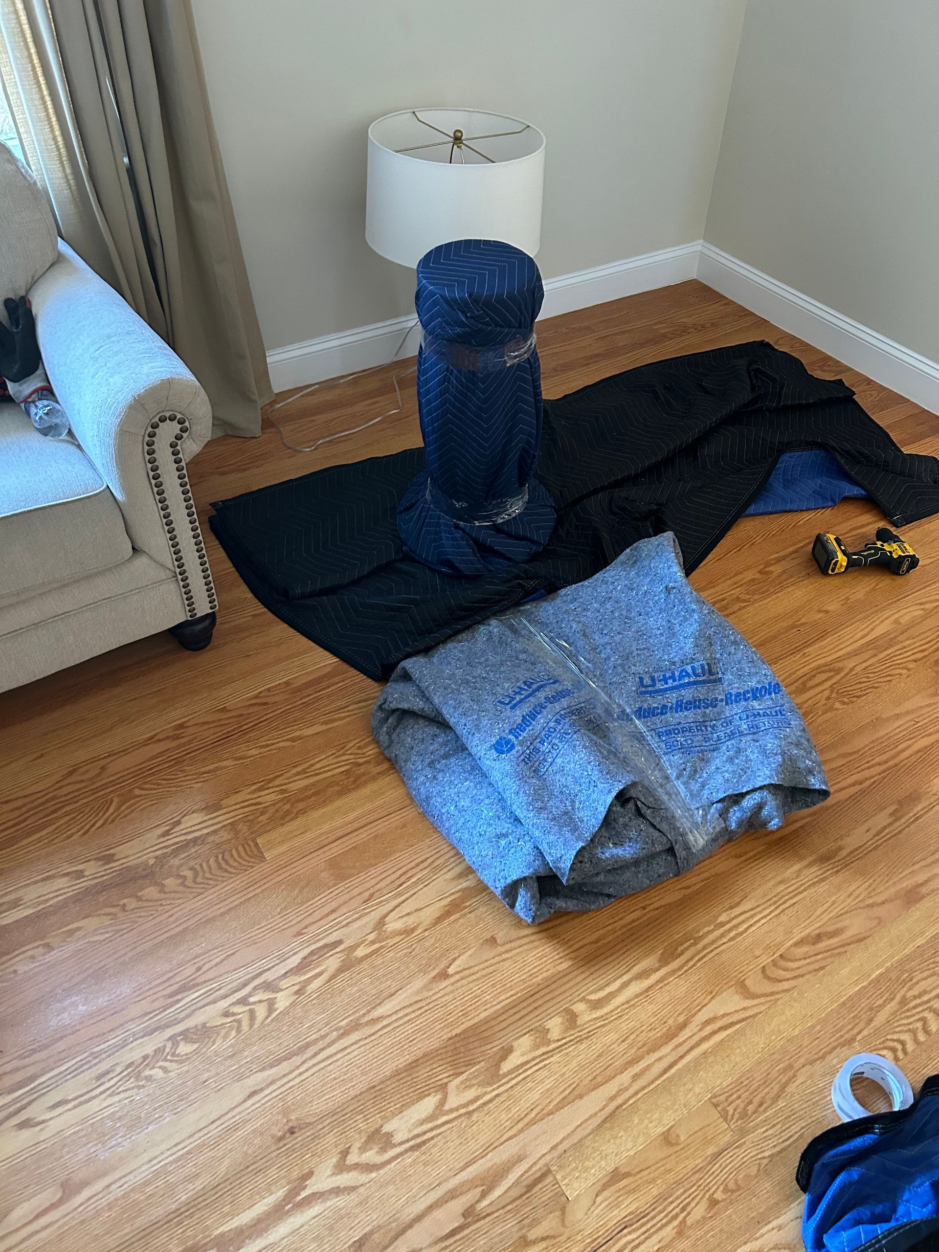 A living room with a couch , chair , and blankets on the floor.