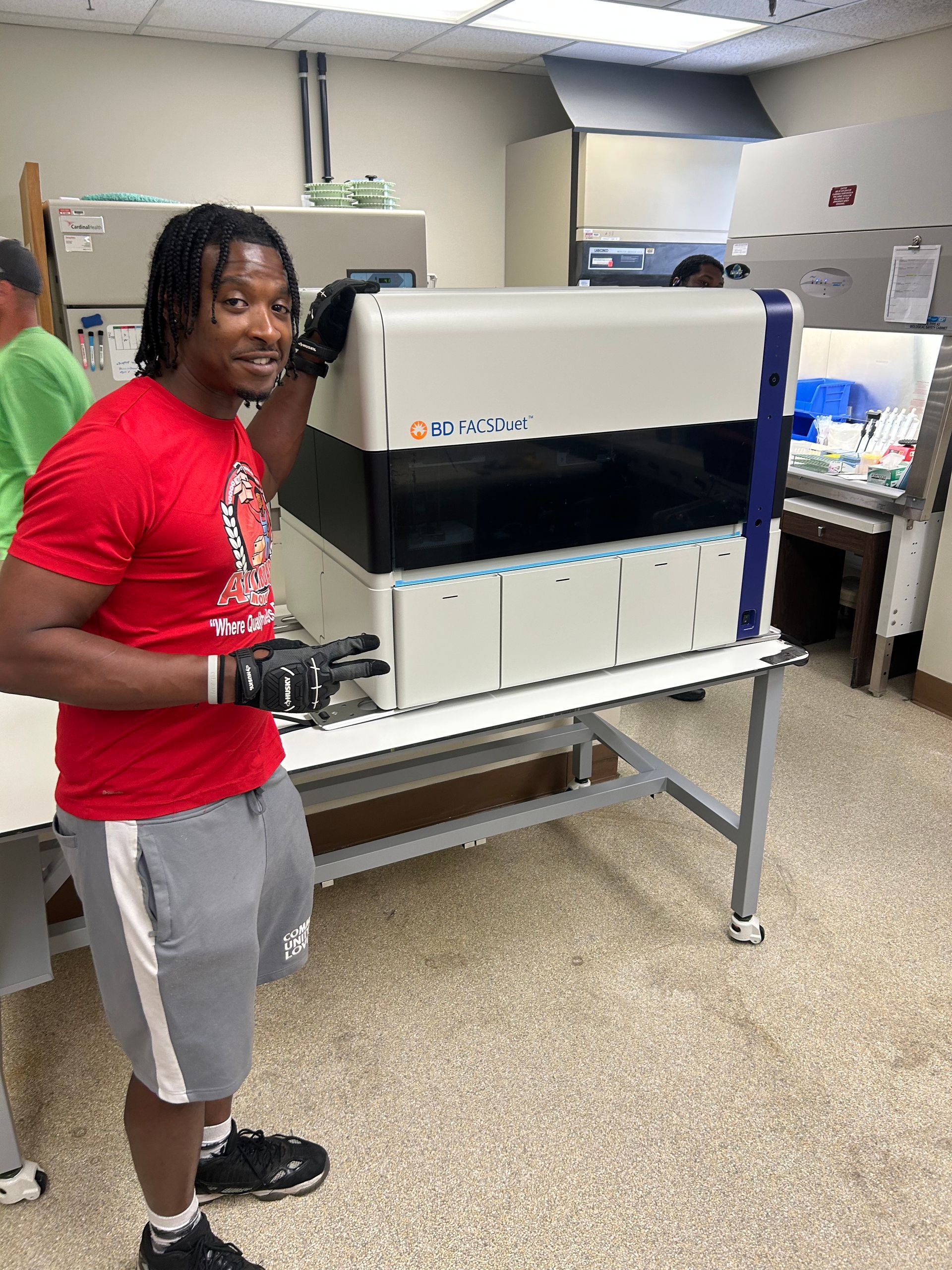 A man in a red shirt is standing next to a machine in a lab.