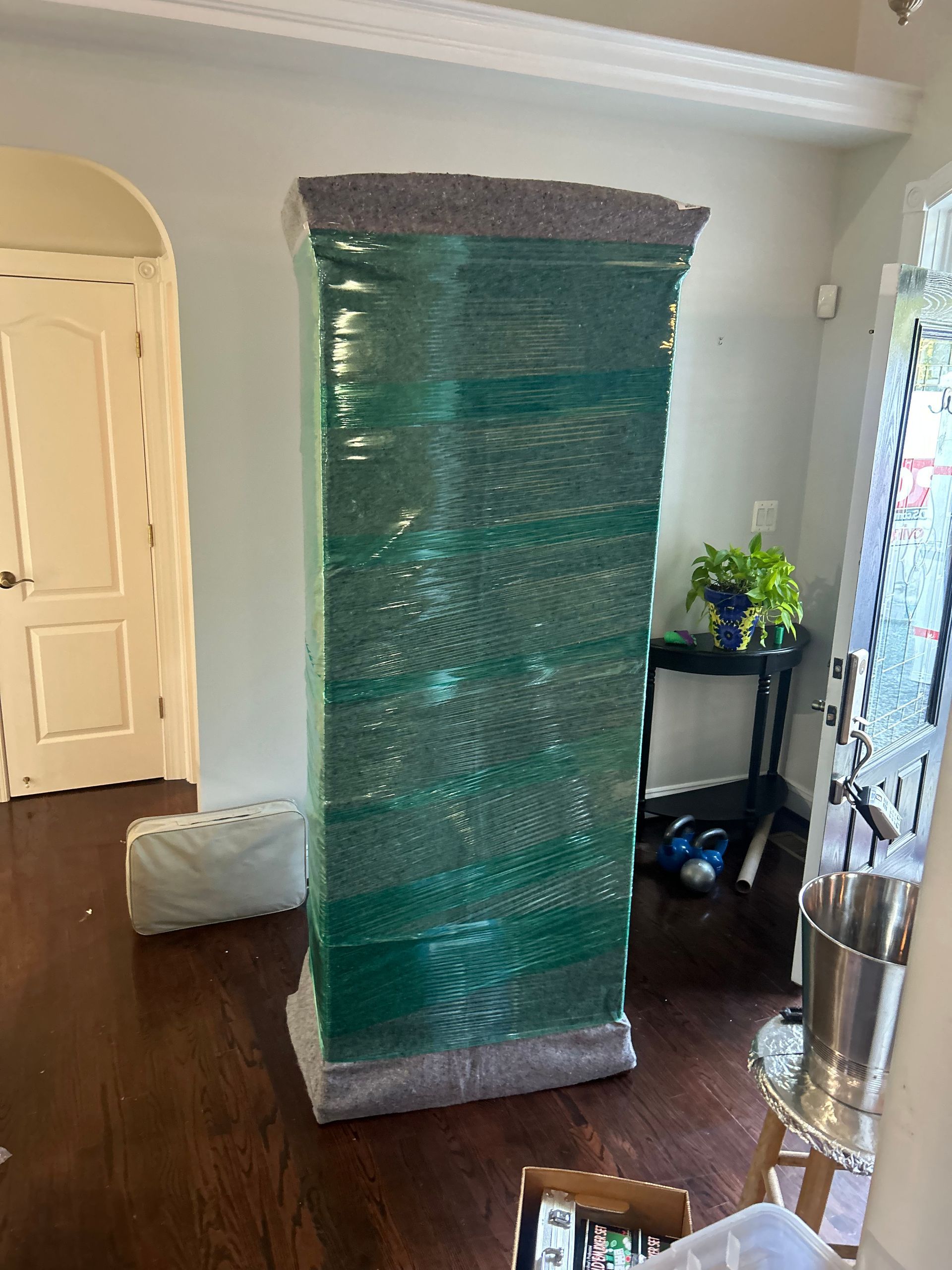 A large green box is wrapped in plastic in a living room.