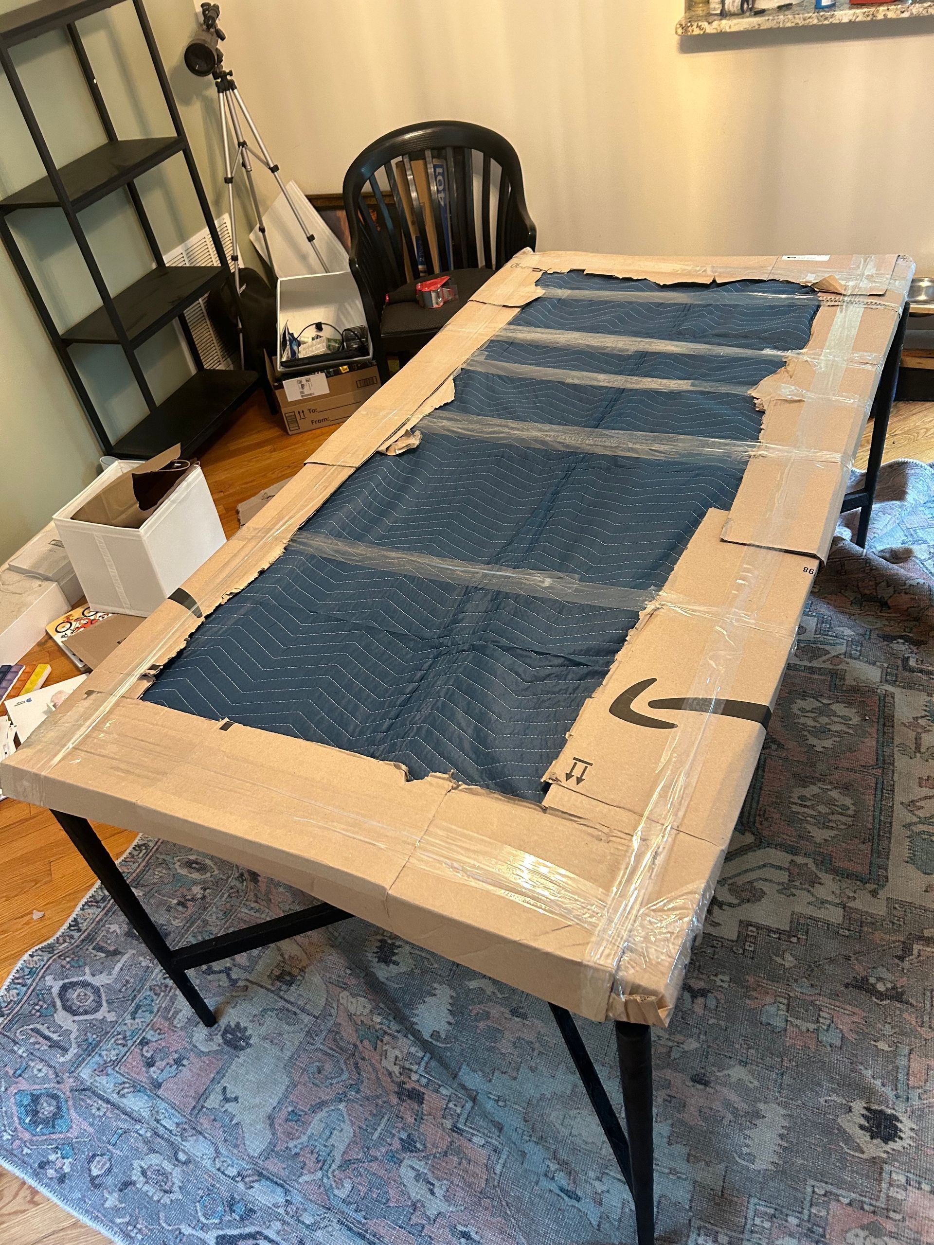A table is wrapped in cardboard and sitting on a rug in a room.