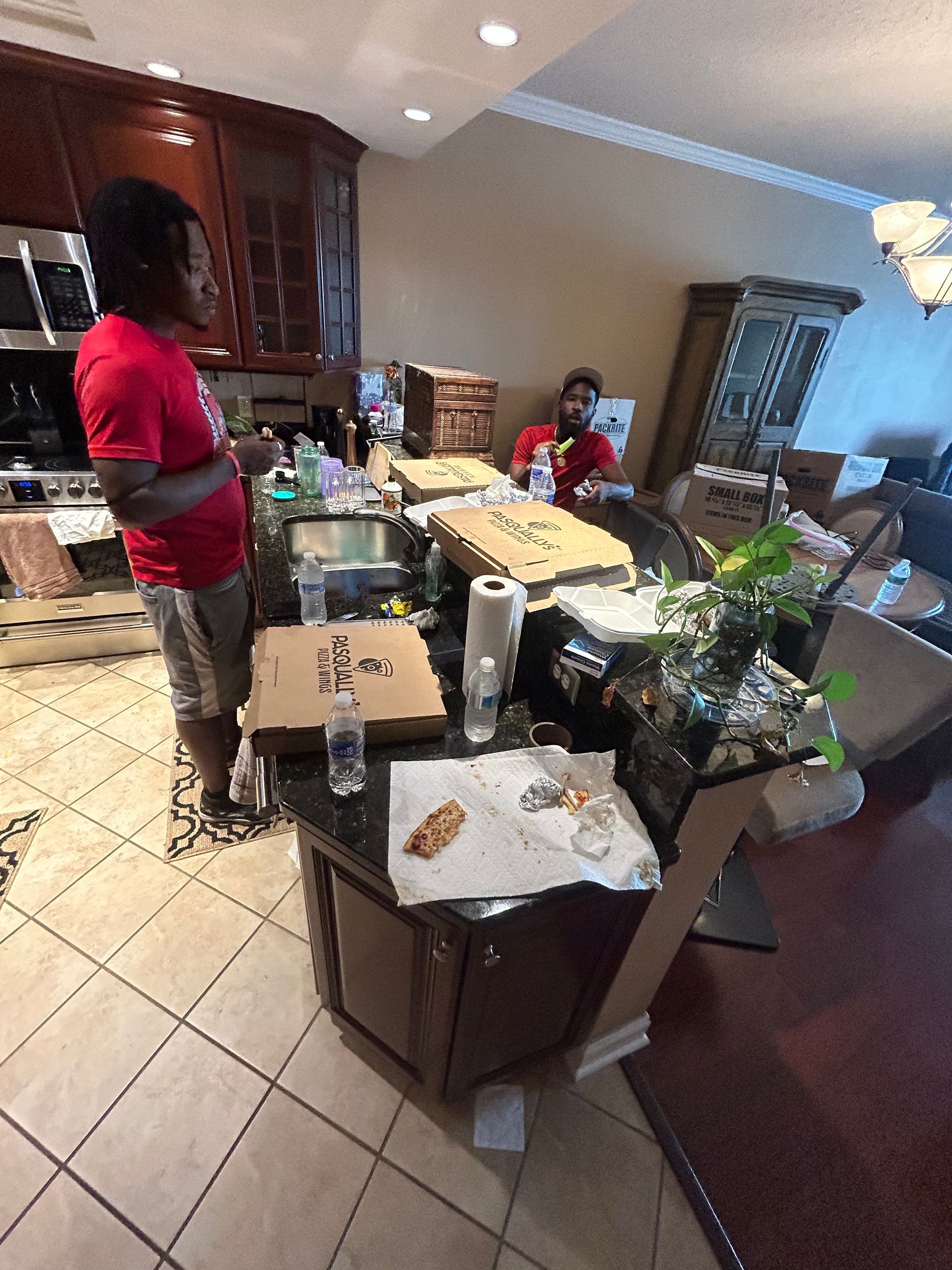 A man in a red shirt is standing in a messy kitchen.