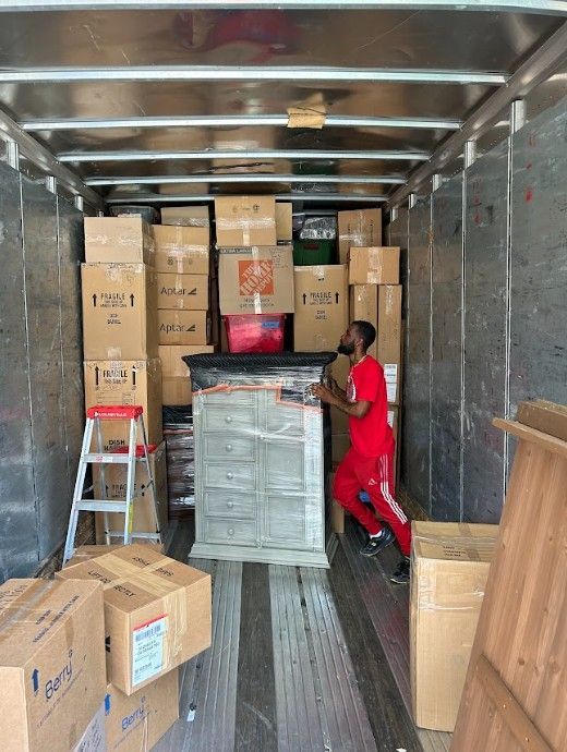 A person loads a truck with boxes and furniture. Inside a moving truck, they appear to be lifting an item.
