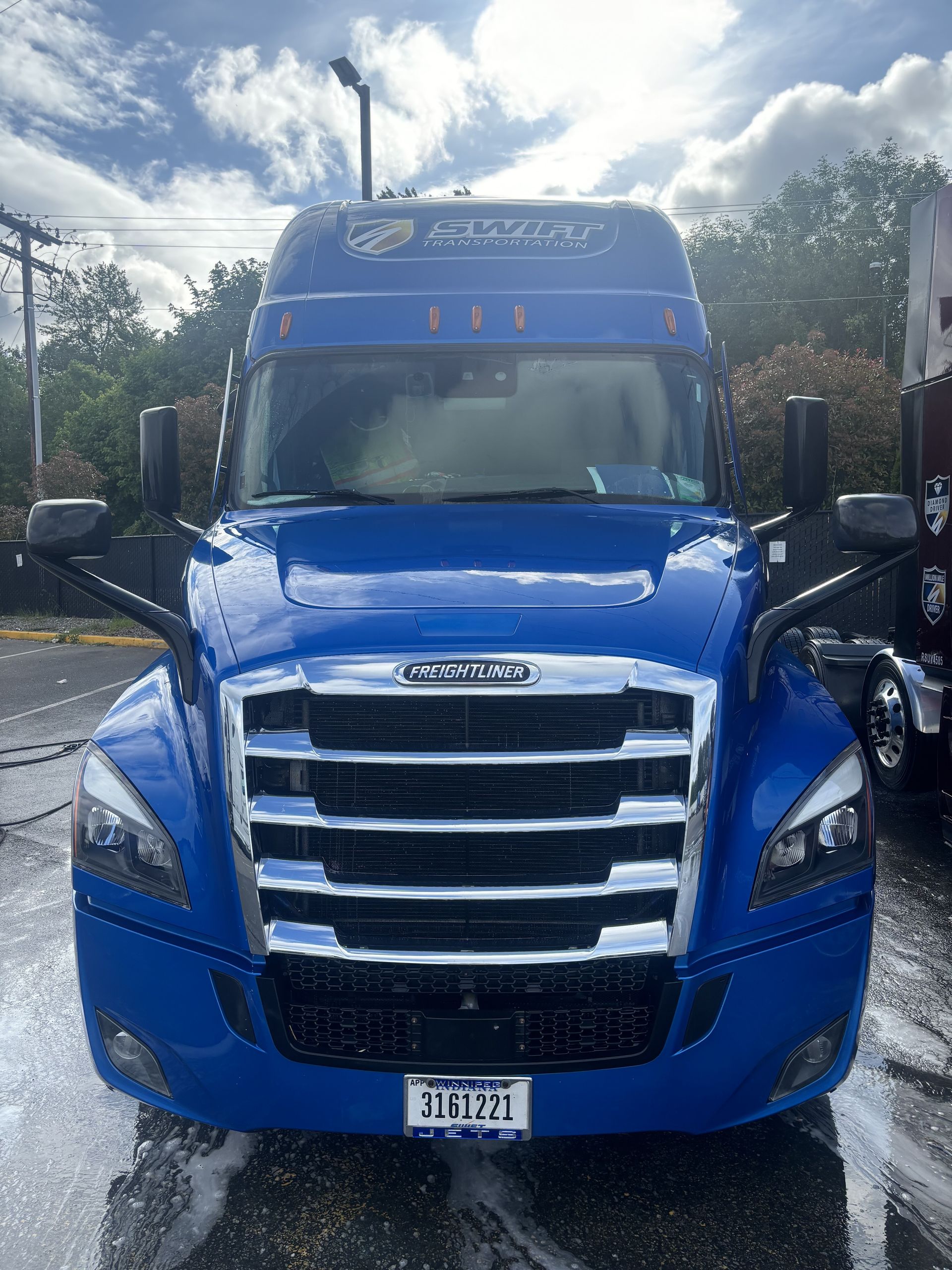 Blue semi-truck with chrome grill and mirrors, parked outside. The front of the vehicle is wet.