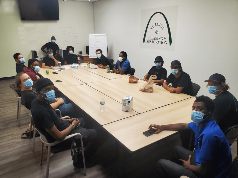 A group of people wearing face masks are sitting around a long table.