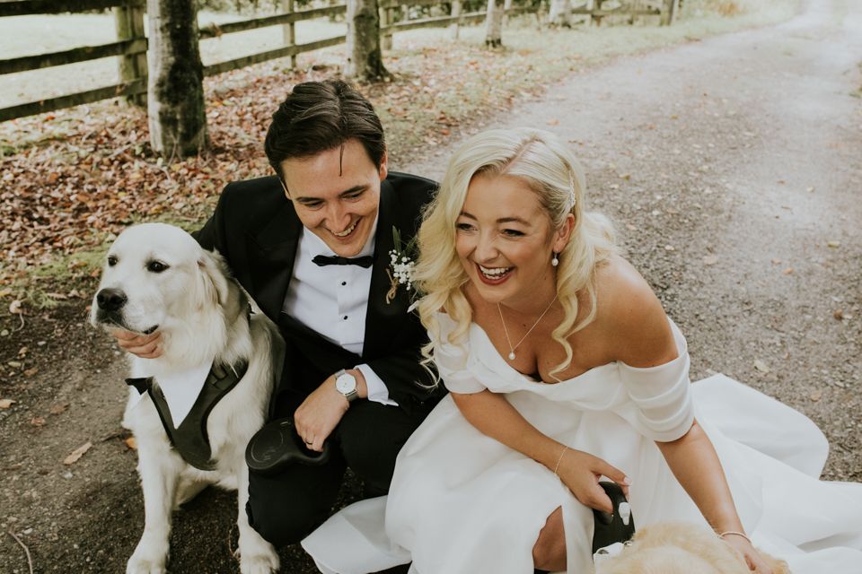 Bride and groom laughing and cuddling pet dog on wedding day