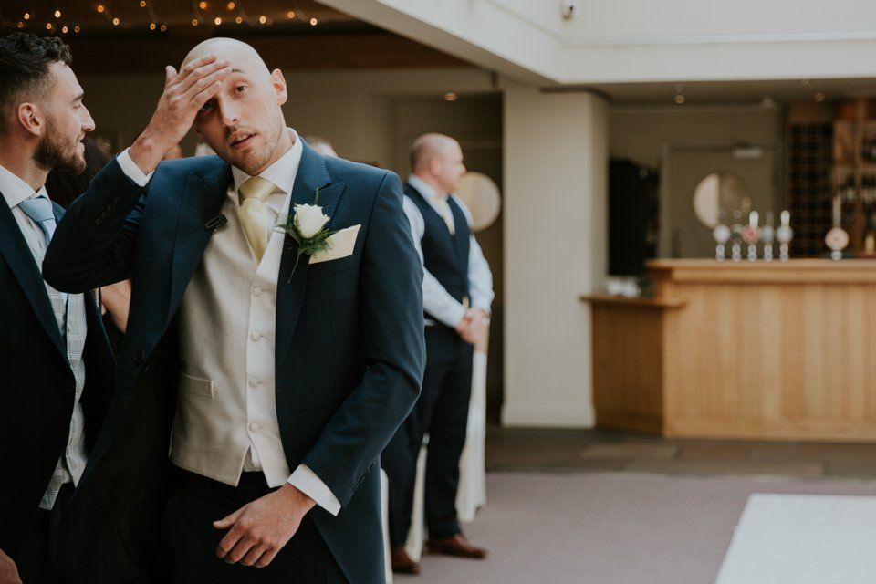 groom holding his head whilst waiting for his bride at the end of the isle at the white hart lydgate