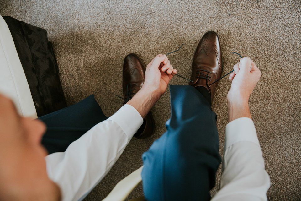 groom tying his shoes before leaving for his wedding