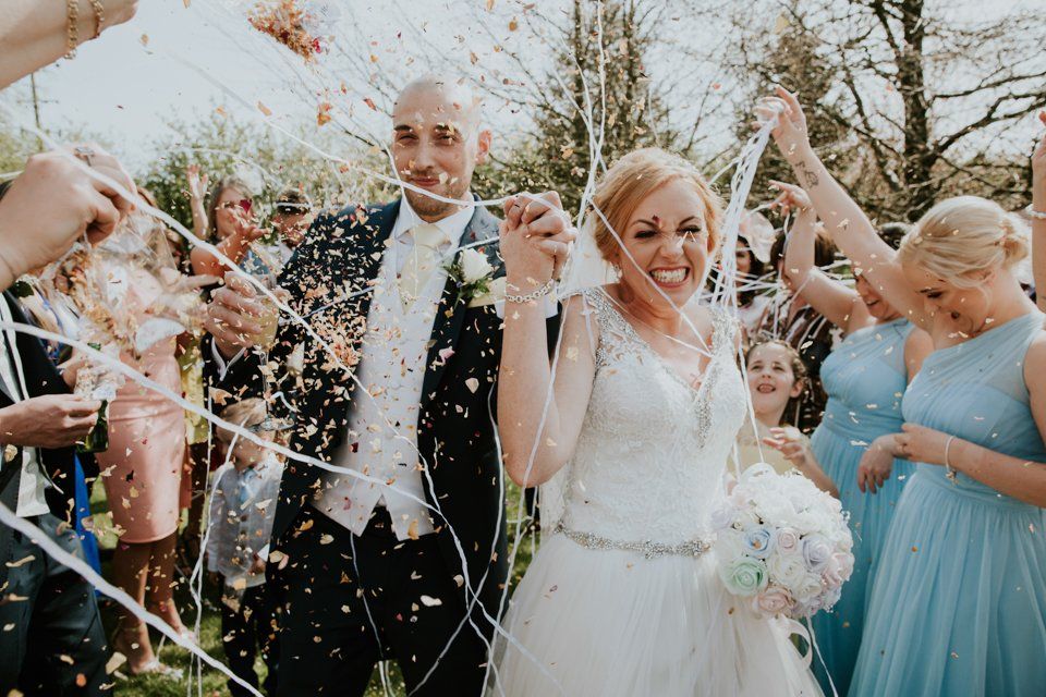 bride and groom holding hands walking through confetti at the white hart lydgate wedding