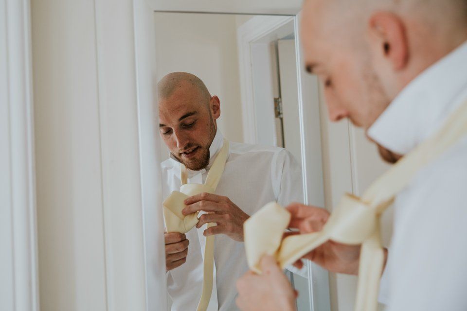 groom doing his tie in the mirror the morning of his wedding