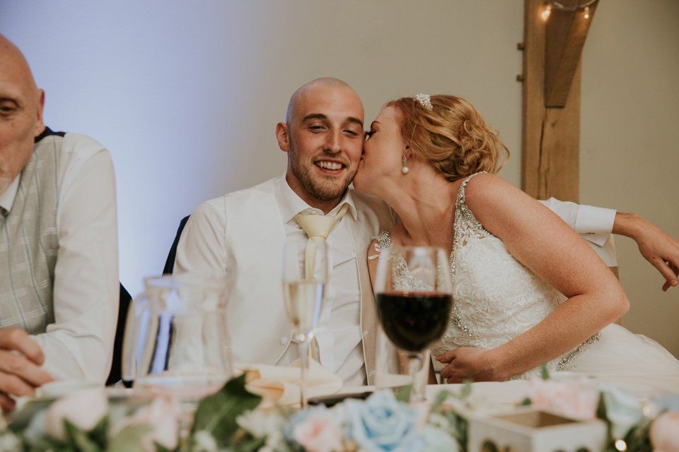 bride kissing groom on the cheek sat at the top table at their wedding
